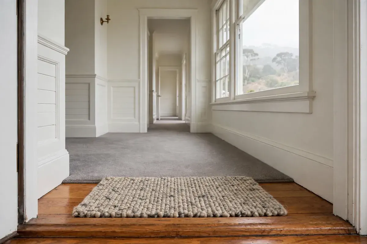 Bungalow entry hall with a doormat and gray carpeted hallway in soft coastal light